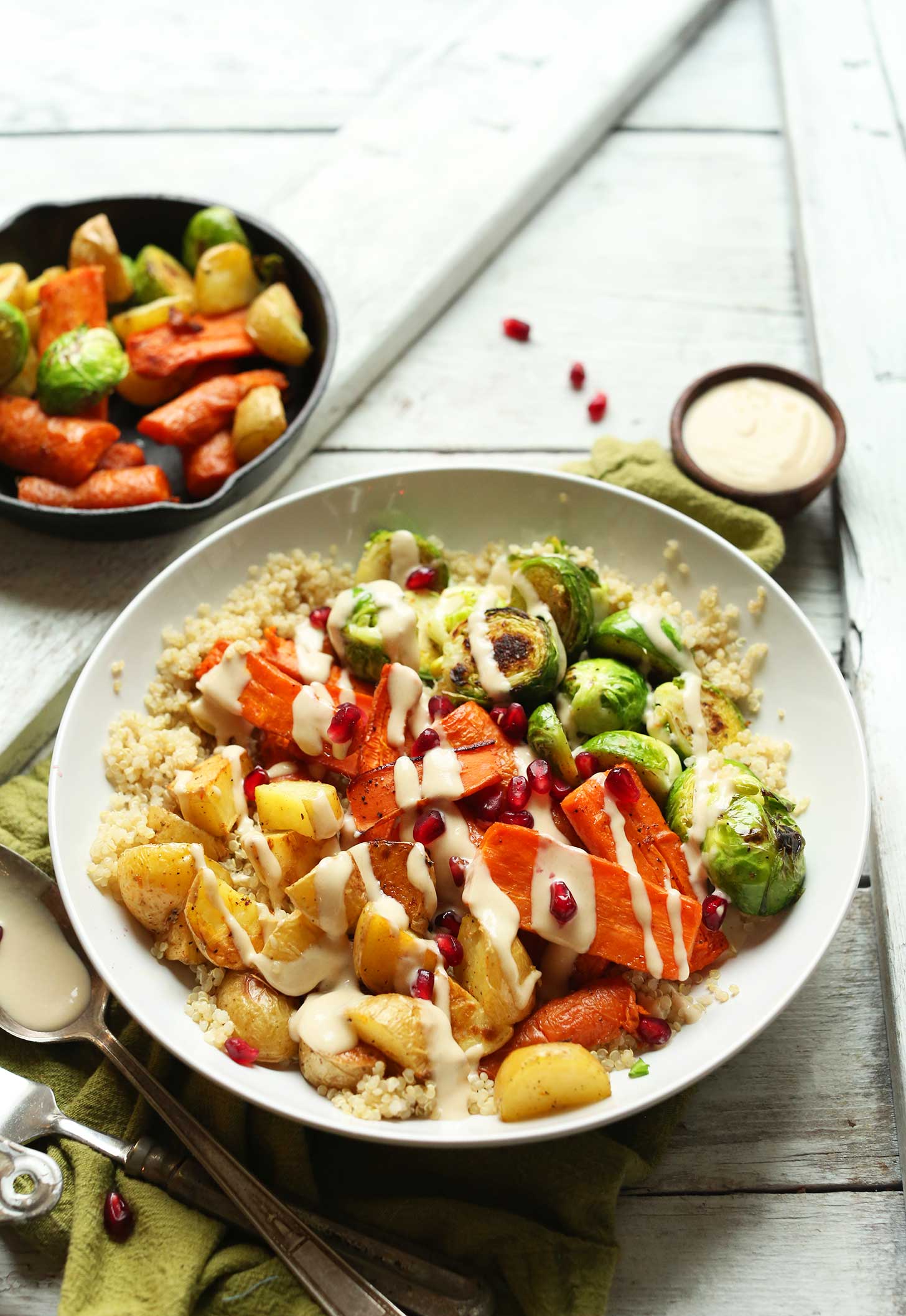Bowl containing a hearty vegan meal of quinoa, roasted vegetables, pomegranate, and dressing