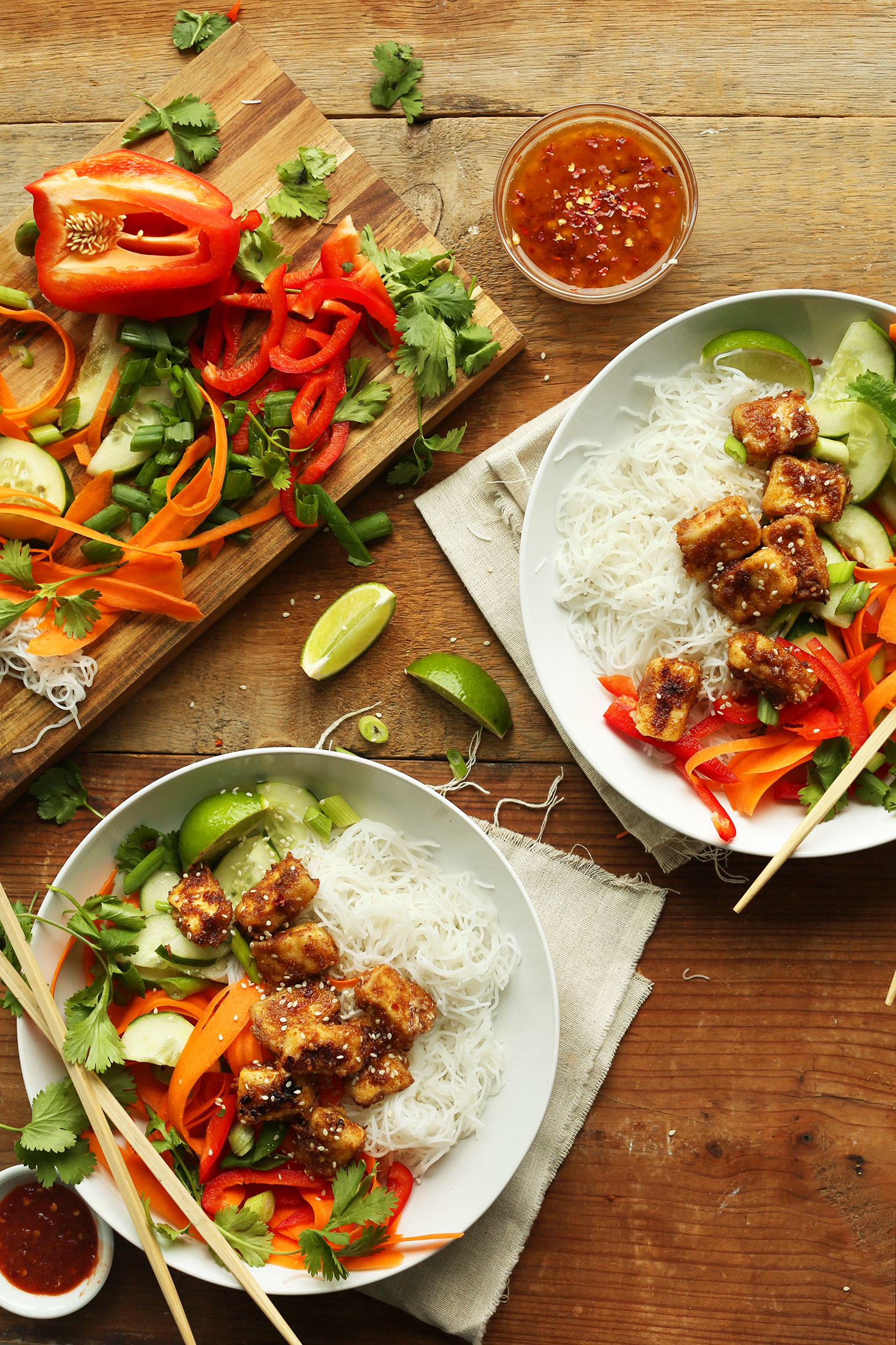 Two Thai Noodle Bowls with Crispy Almond Butter Tofu alongside a cutting board with ingredients used to make the recipe