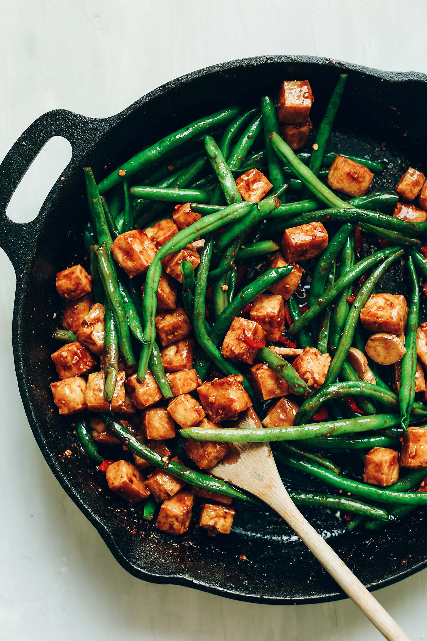 Using a wooden spoon to stir Almond Butter Tofu Stir-Fry in a cast iron skillet