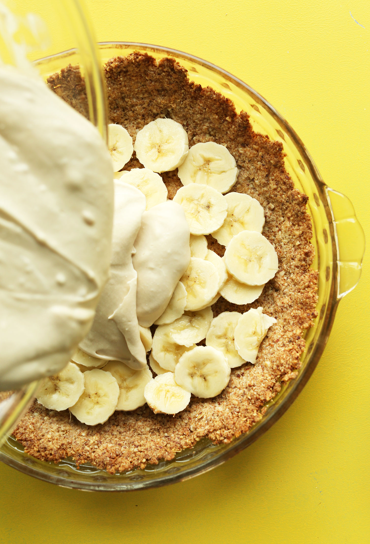 Pouring filling over the crust and banana layers for our gluten-free vegan Banana Cream Pie