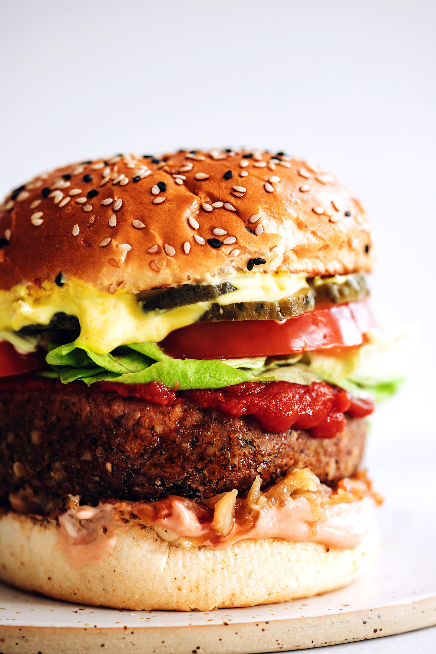 Close up shot of a bun with pickles, mustard, tomato, lettuce, ketchup, vegan burger patty, caramelized onions, and sriracha mayo
