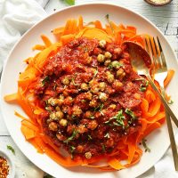Gold spoon and fork resting on a plate of Chickpea Bolognese over Carrot Noodles
