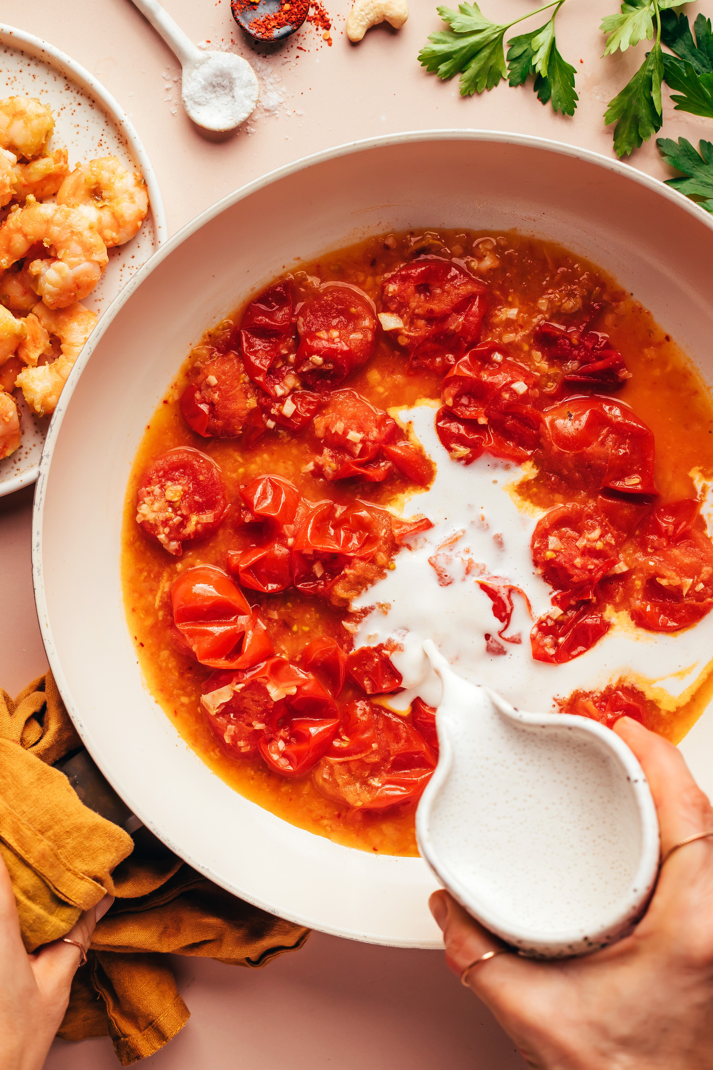 Pouring cashew cream into a skillet of burst tomatoes