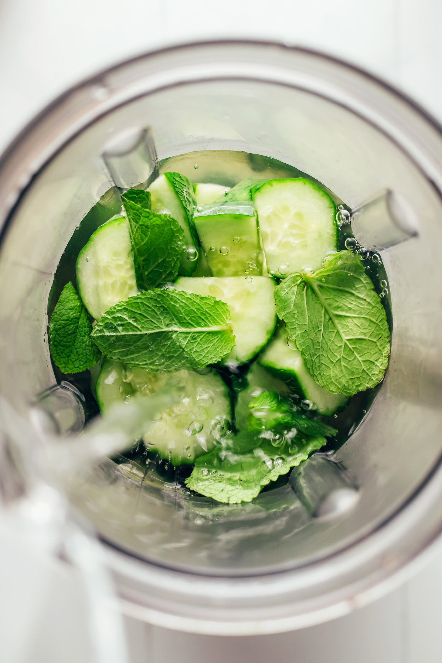 Pouring water into a blender over cucumber slices and fresh mint