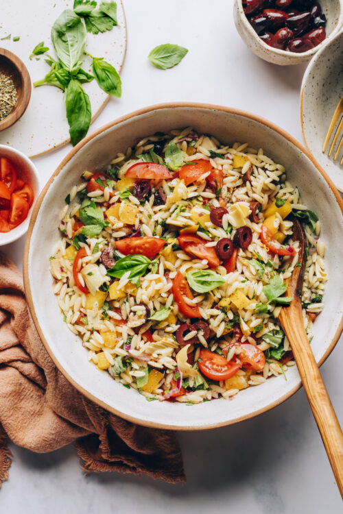Wooden spoon in a bowl of our vegan orzo pasta salad