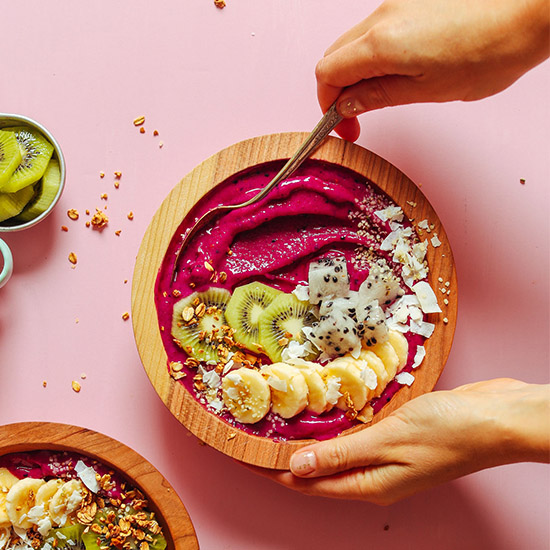 Using a spoon to scoop up a bite of a delicious Dragon Fruit Smoothie Bowl topped with fresh fruit