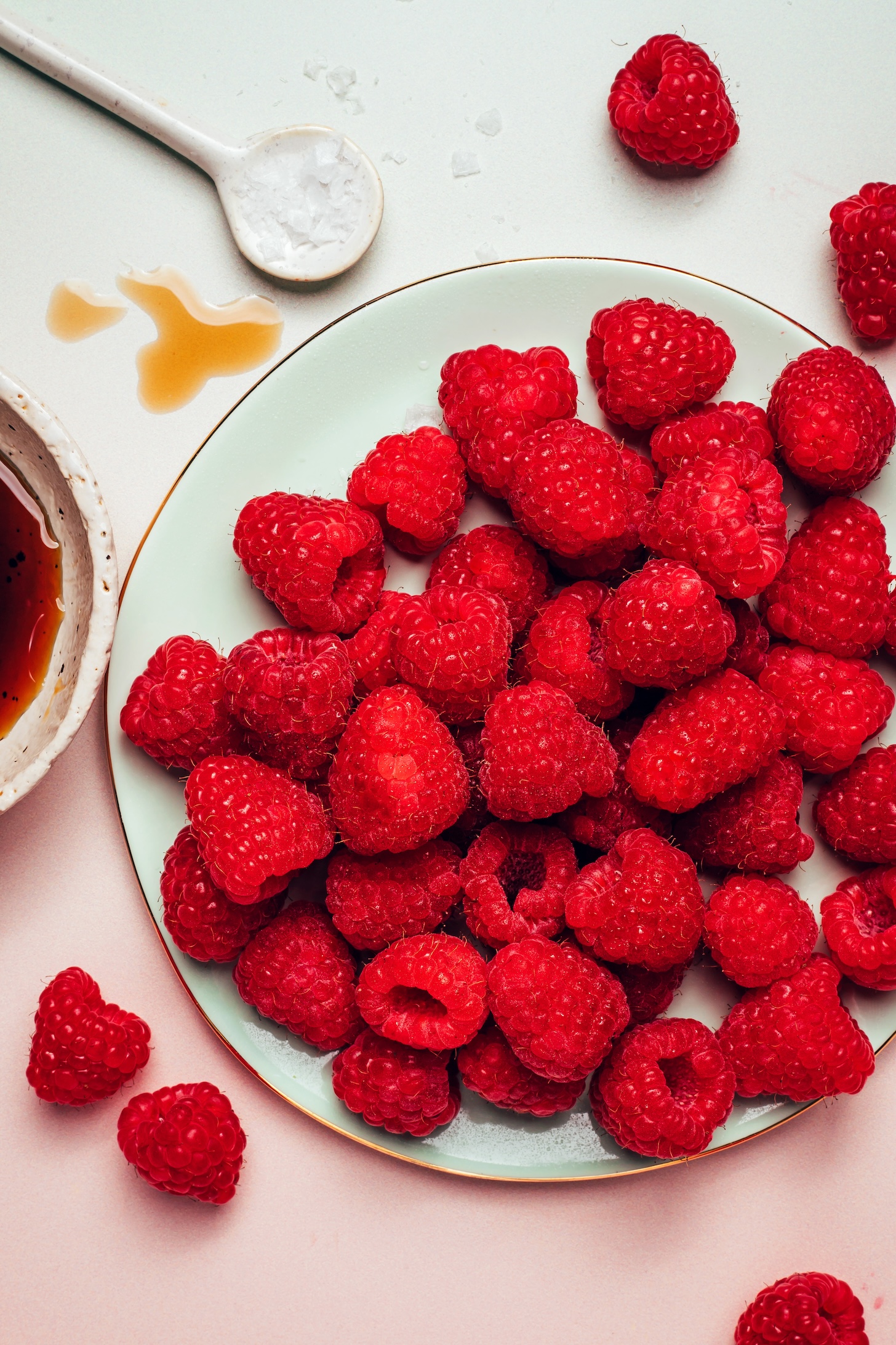 Plate of fresh raspberries with a spoonful of sea salt and bowl of maple syrup next to it