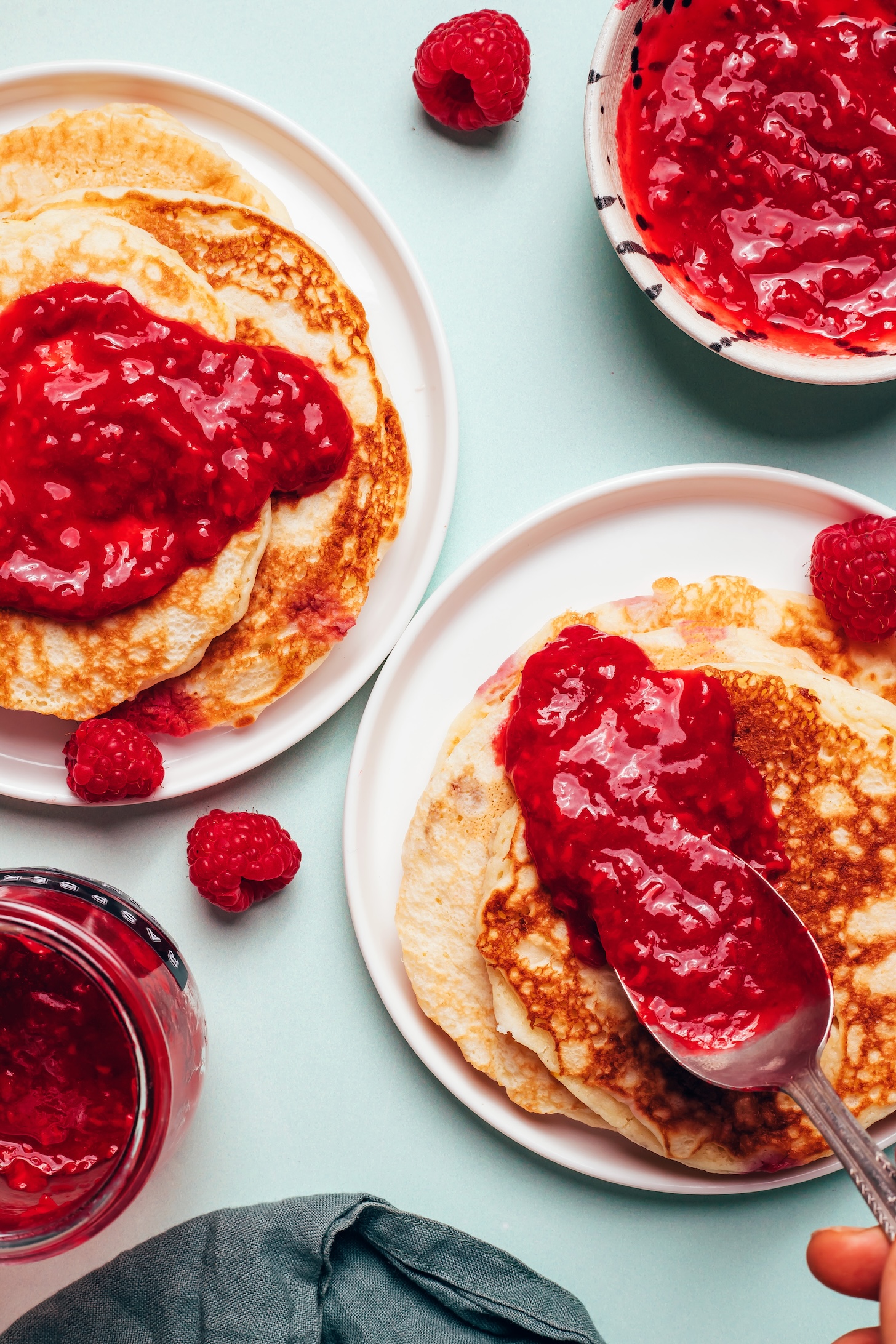 Using a spoon to add raspberry compote on top of a stack of crepes