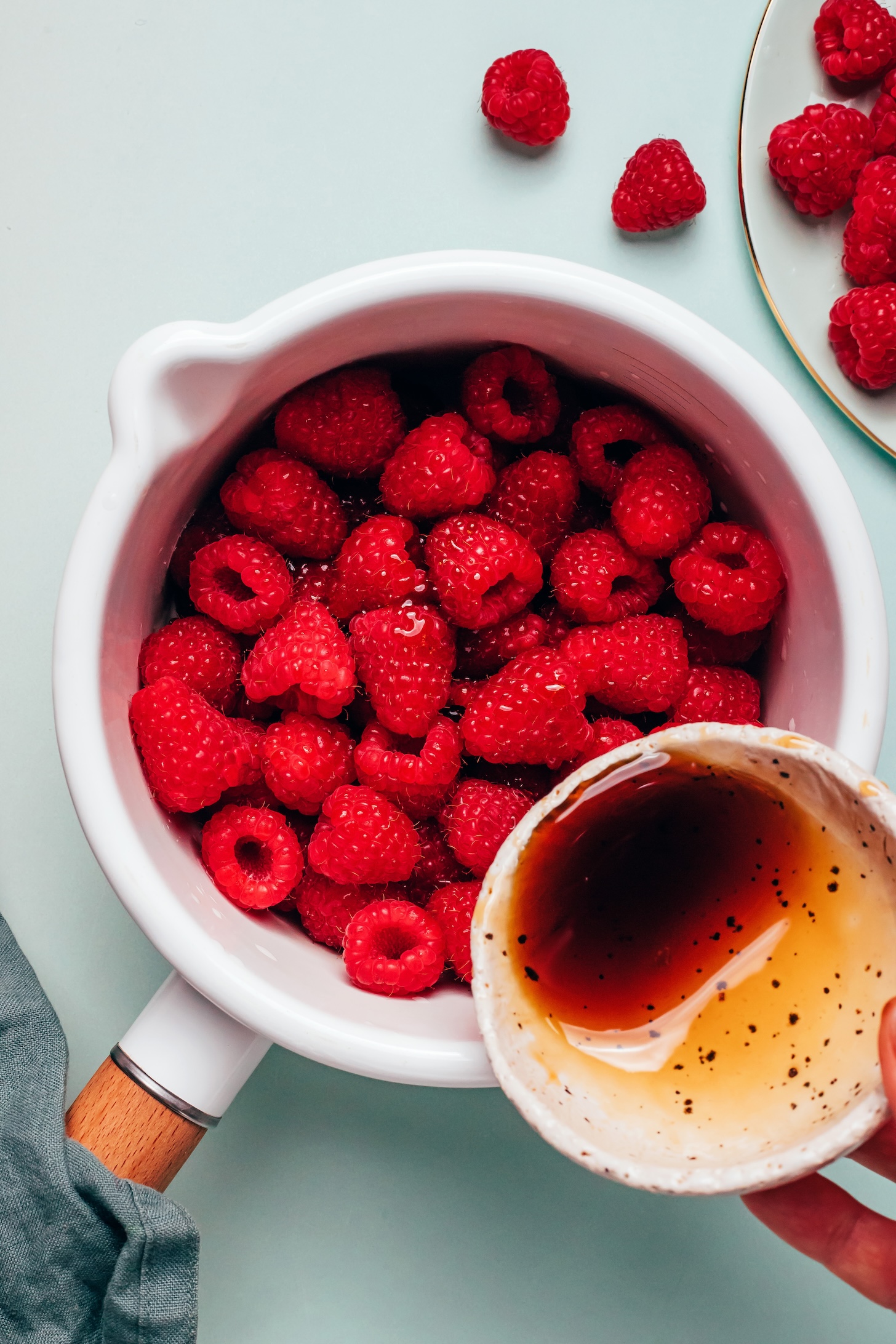 Pouring maple syrup into a saucepan of fresh raspberries