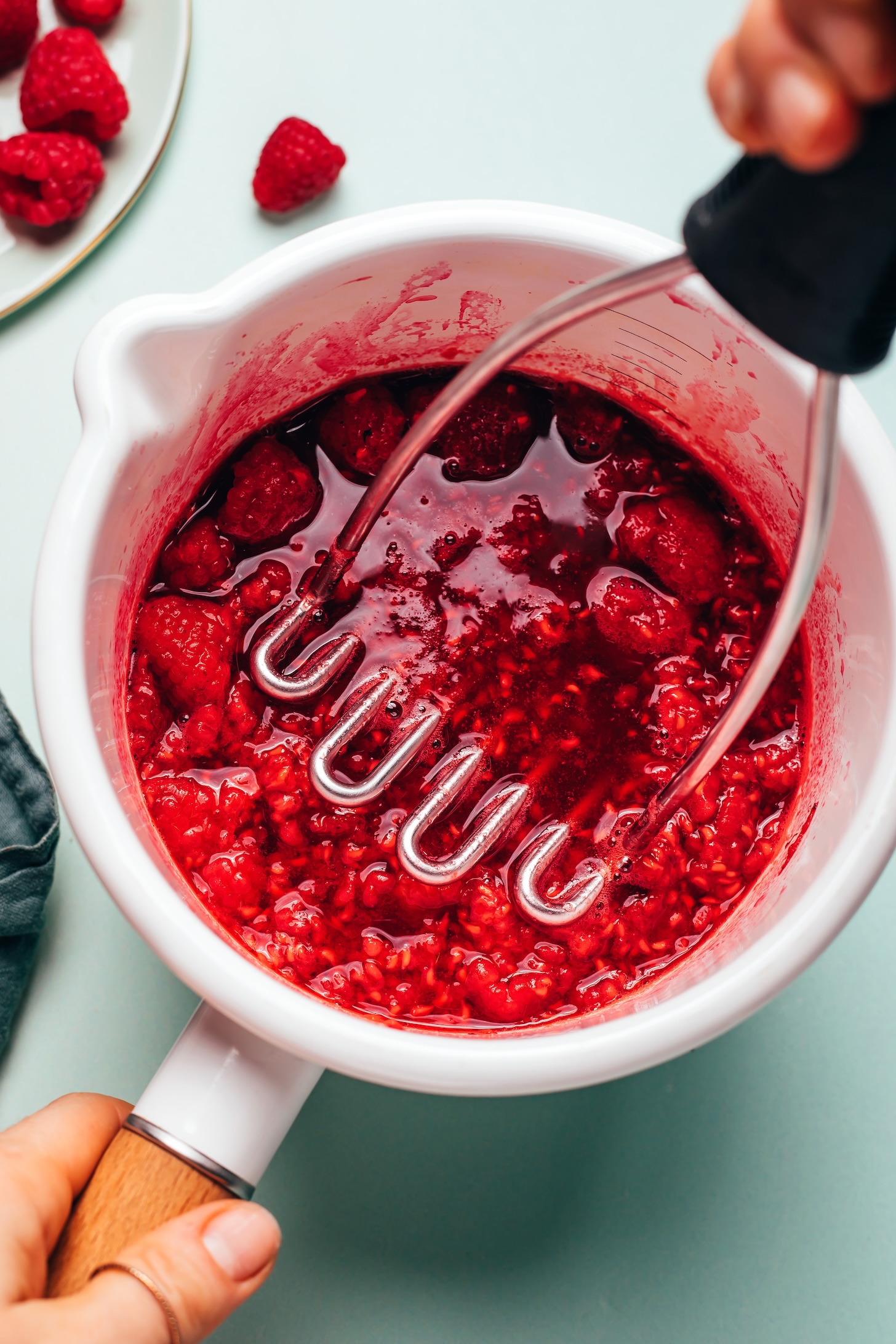 Using a potato masher to mash raspberry compote in a saucepan
