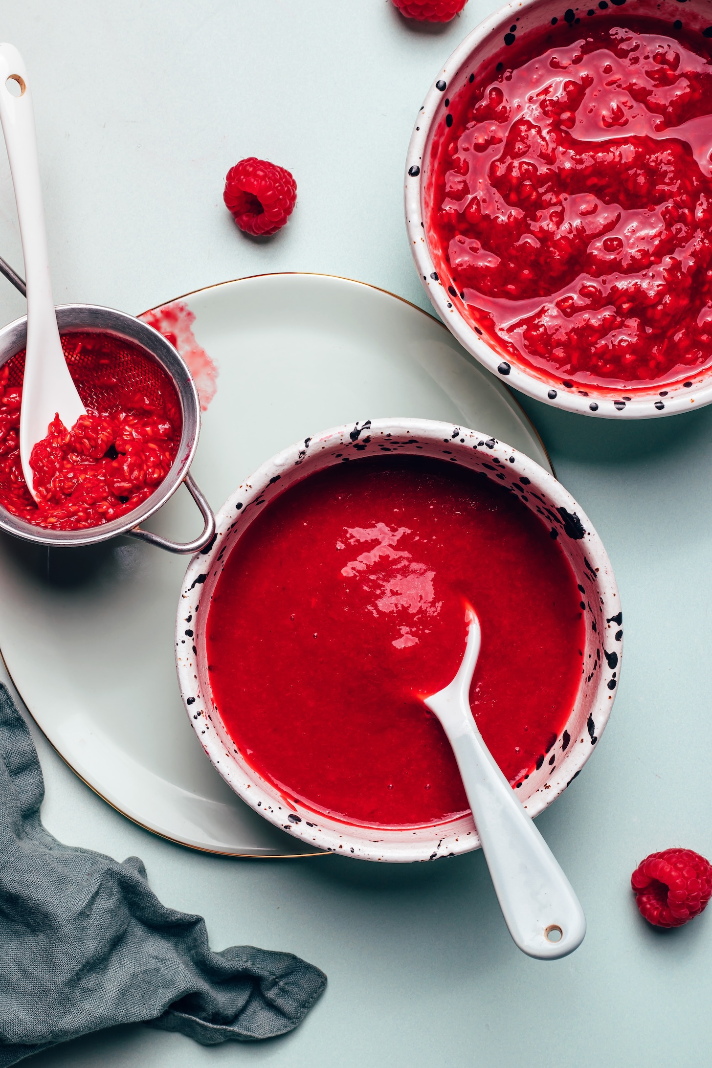 Bowls of raspberry compote with and without seeds and a strainer used for removing the seeds