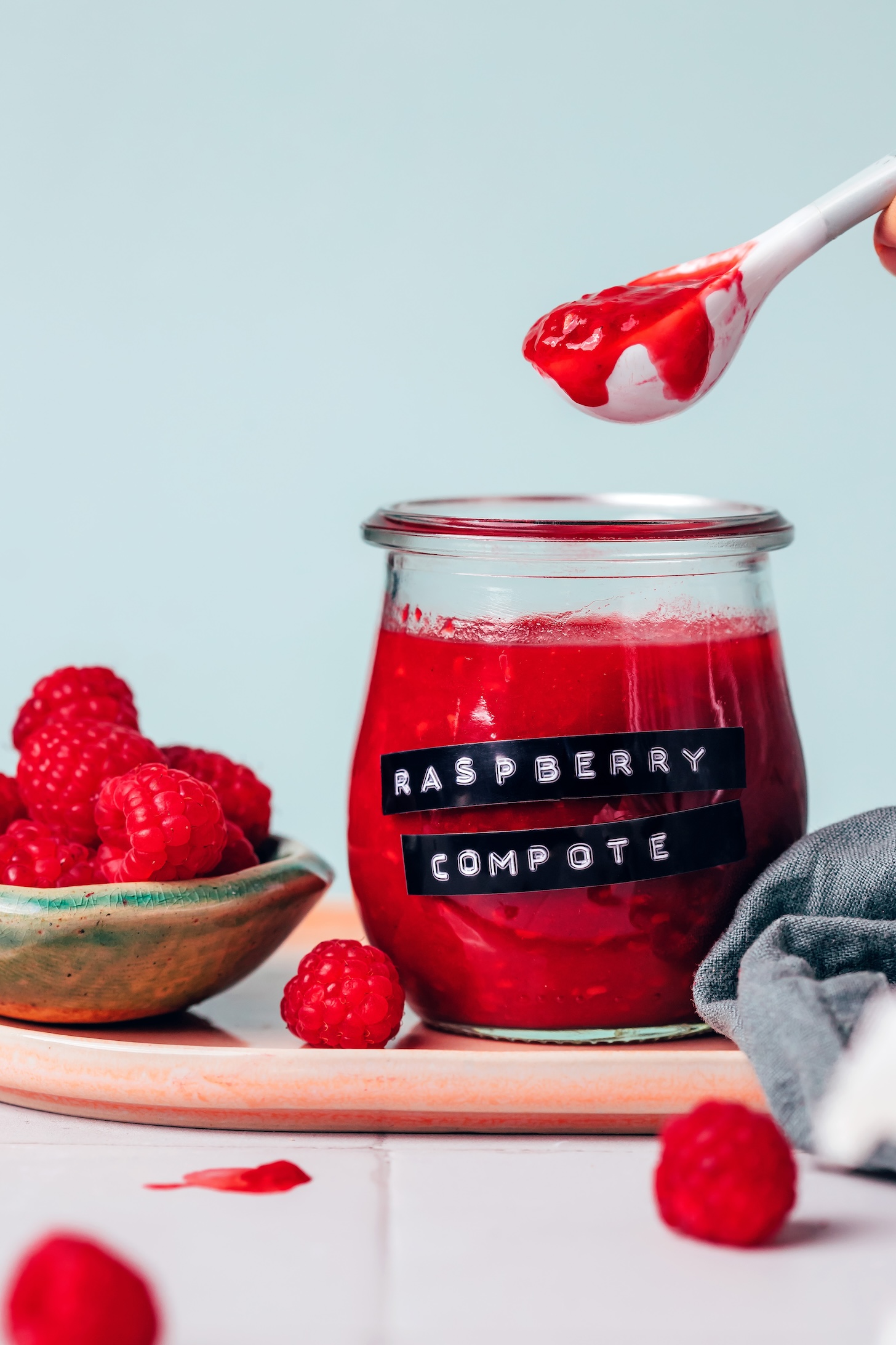 Spoonful of raspberry compote over a jar of compote with fresh raspberries next to it