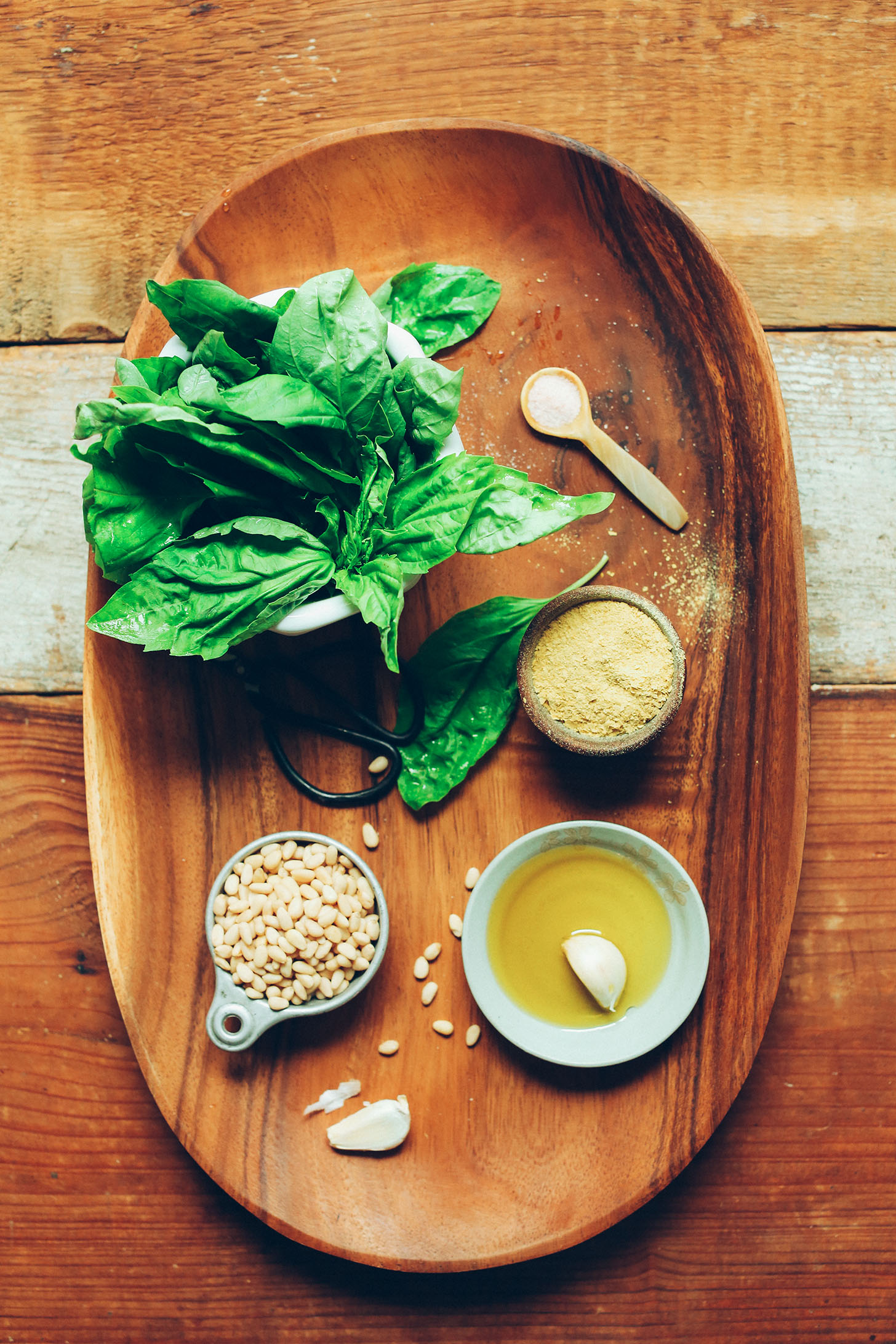 Wood platter with fresh basil, nutritional yeast, pine nuts, olive oil, garlic, and salt for making our homemade vegan pesto recipe