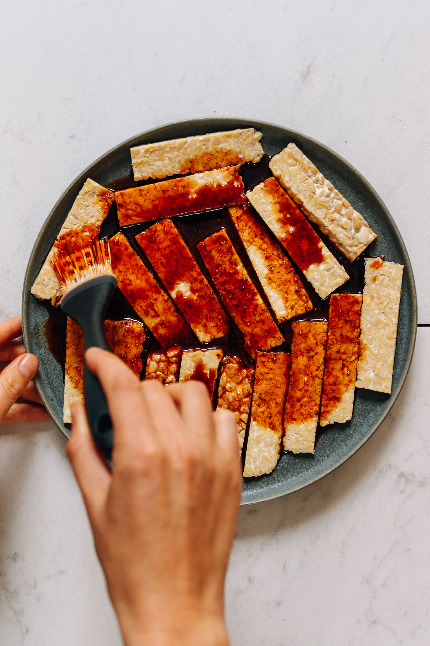 Using a pastry brush to spread marinade on tempeh bacon