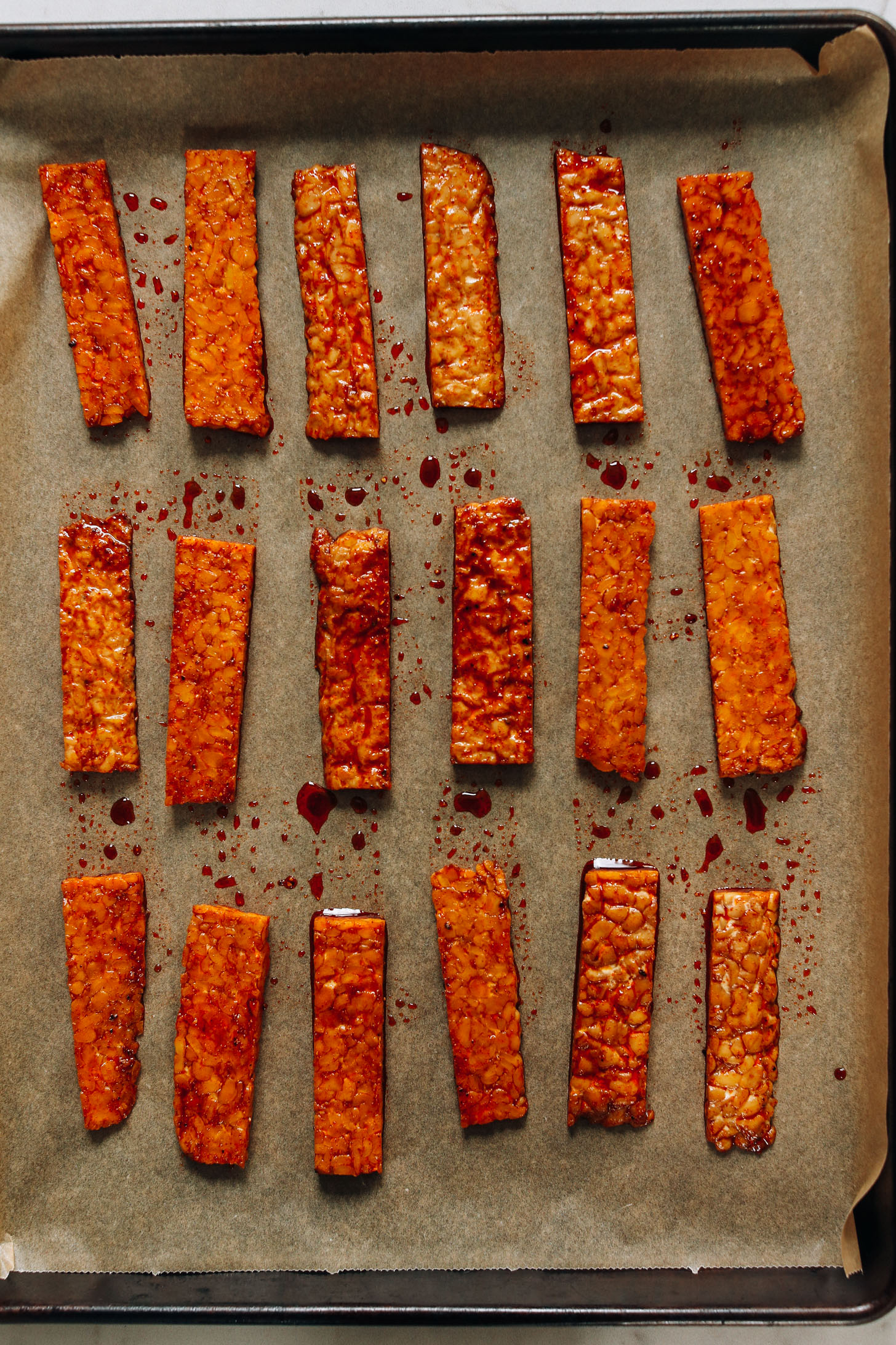 Baking sheet with thinly sliced strips of tempeh coated in a marinade