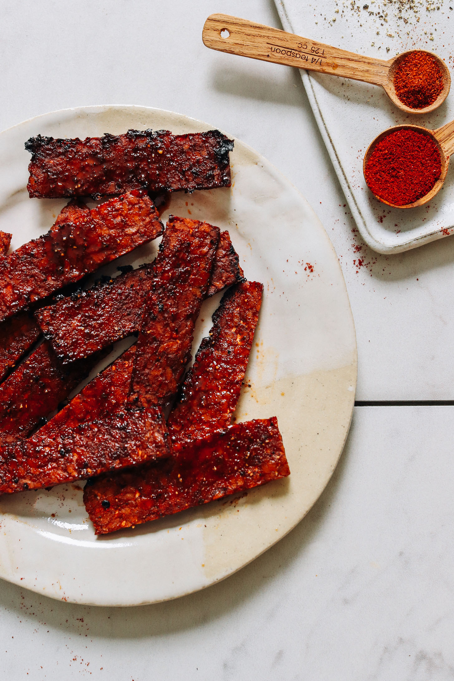 Spices next to a plate of vegan tempeh bacon slices