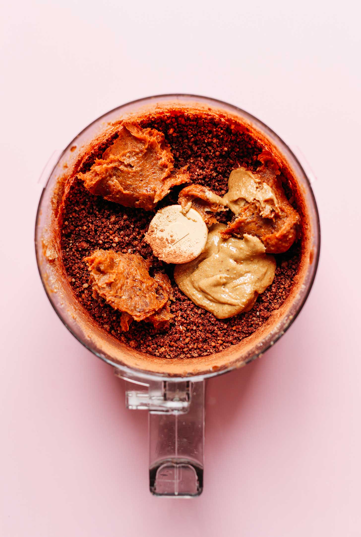 Adding nut butter to a food processor full of vegan Dark Chocolate energy bites
