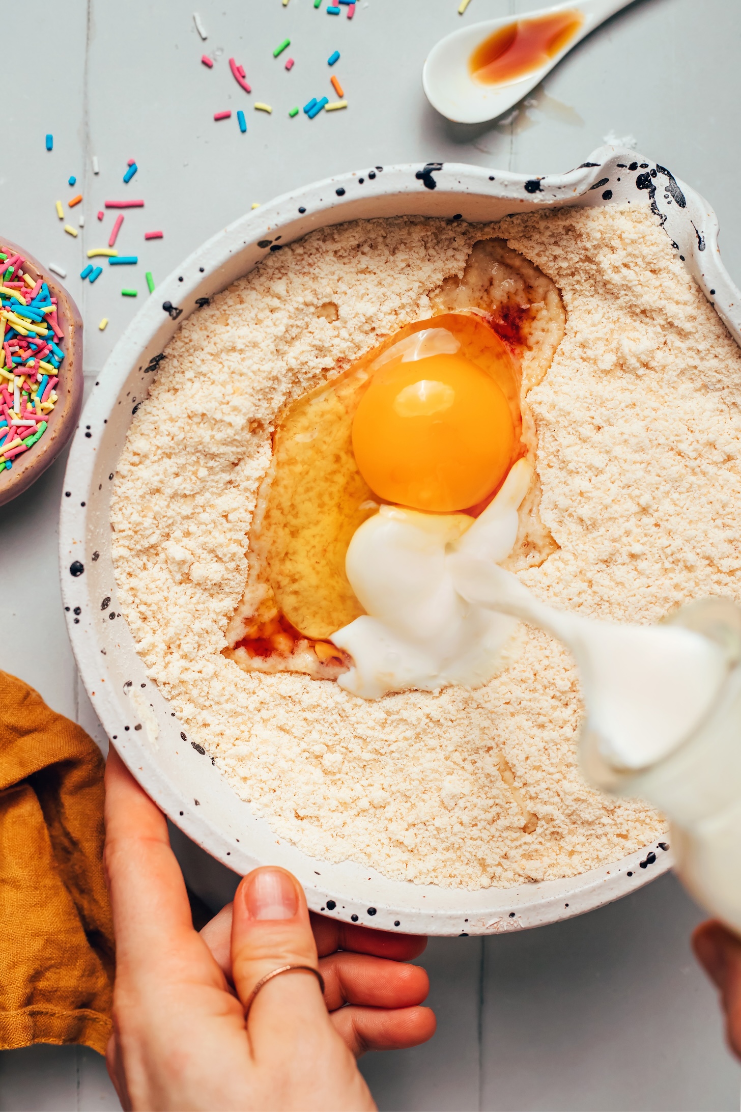 Pouring dairy-free milk into a bowl with egg and gluten-free flours
