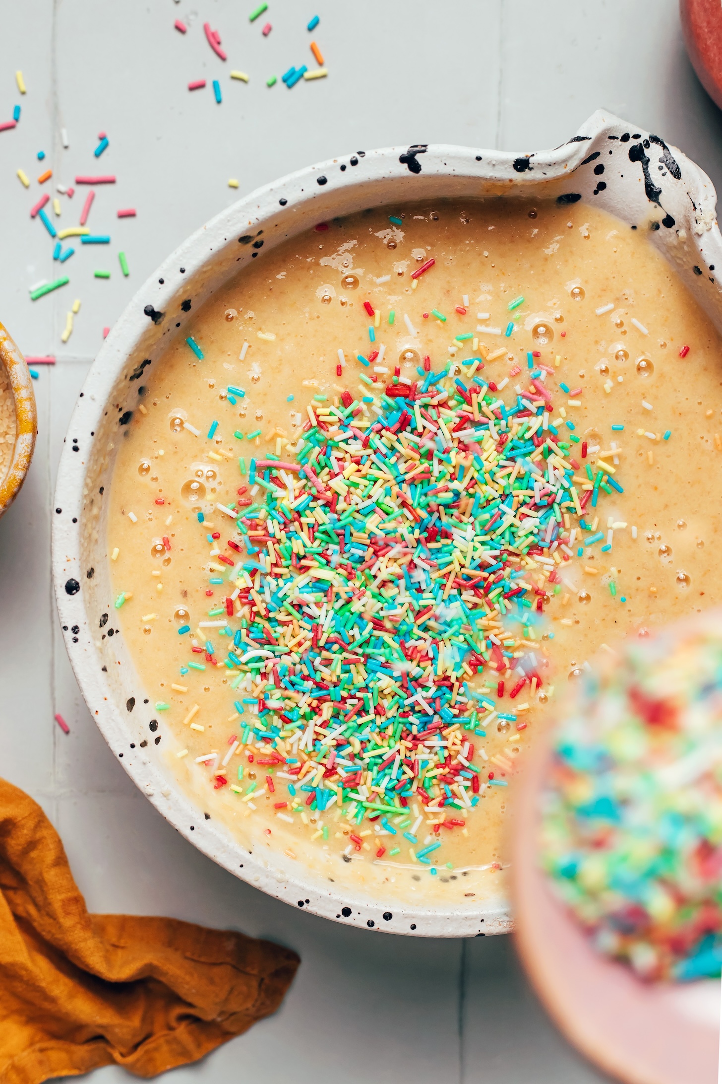Adding rainbow sprinkles into a bowl of funfetti cupcake batter