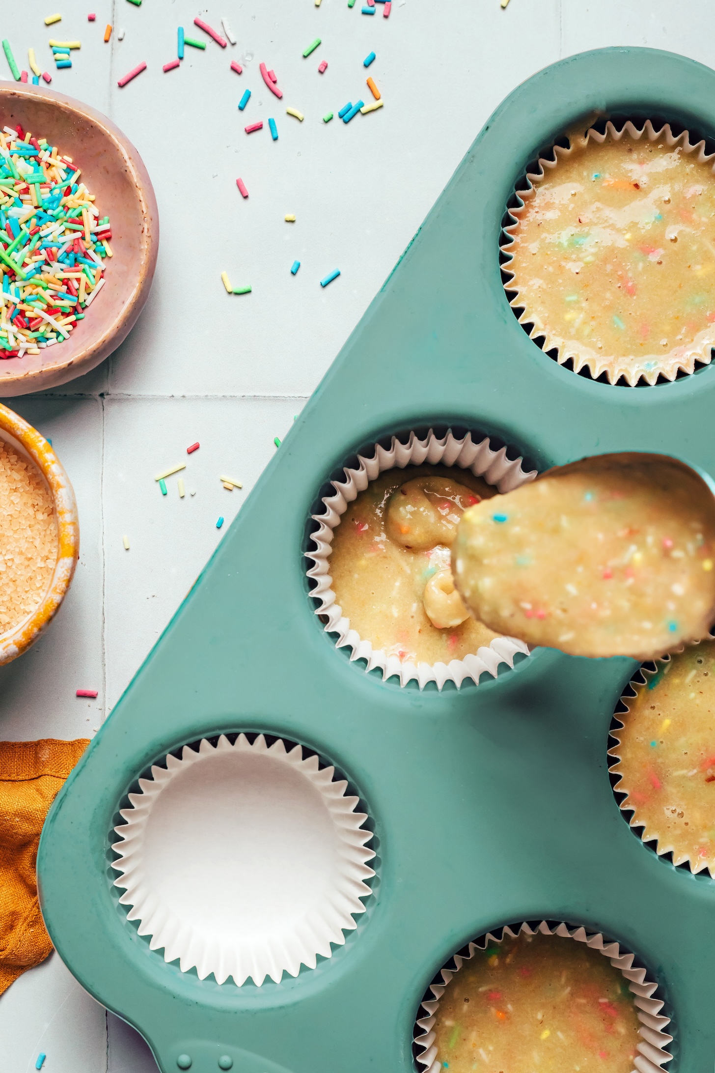 Pouring cupcake batter from a spoon into a parchment-lined muffin tin
