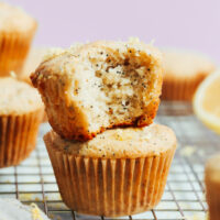 Stack of vegan gluten-free lemon poppy seed muffins with the top one partially eaten to show the fluffy inner texture