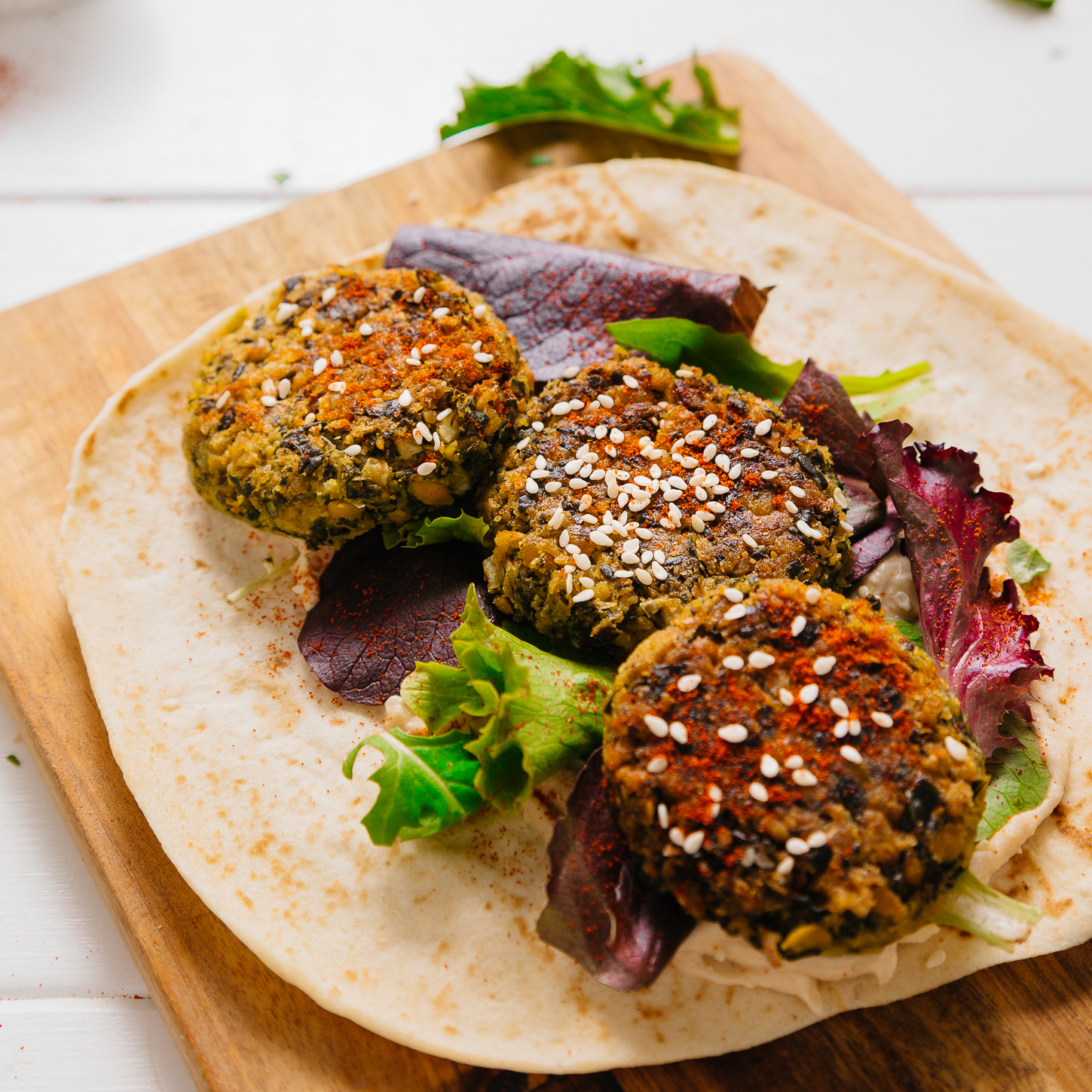 Making a healthy vegan Kale Falafel Hummus Wrap on a wood cutting board