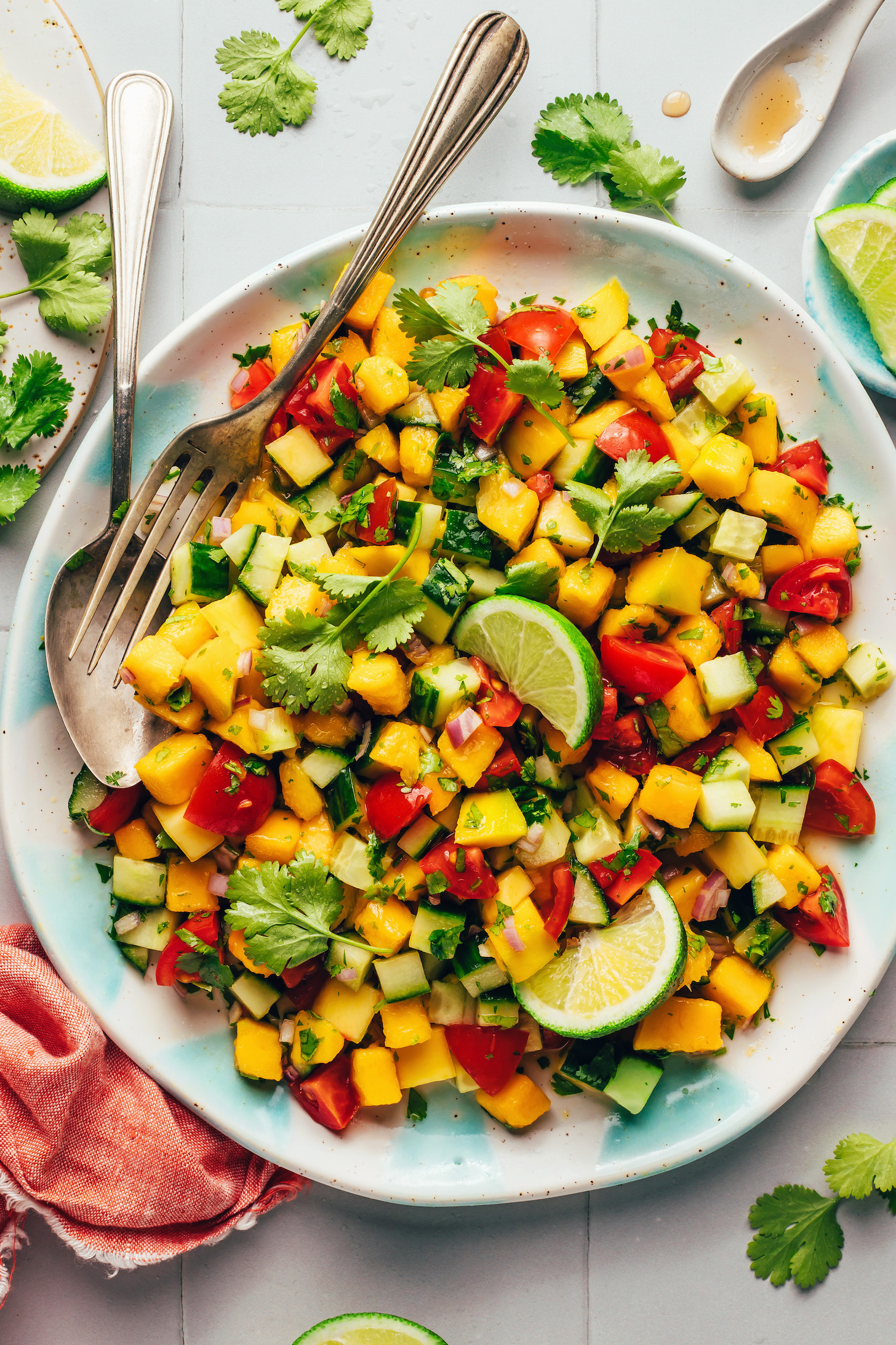 Fork and spoon resting in a bowl of Mango Cucumber Salad with lime wedges on top
