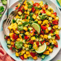 An overhead photo of a spoon and fork in a bowl of mango cucumber salad