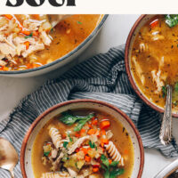 Bowls and Dutch oven of our nourishing chicken noodle soup that can be made classic or with immune-boosting ingredients