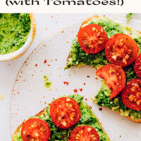 Slices of vegan pesto avocado toast with fresh tomatoes and a bowl of vegan pesto on the side