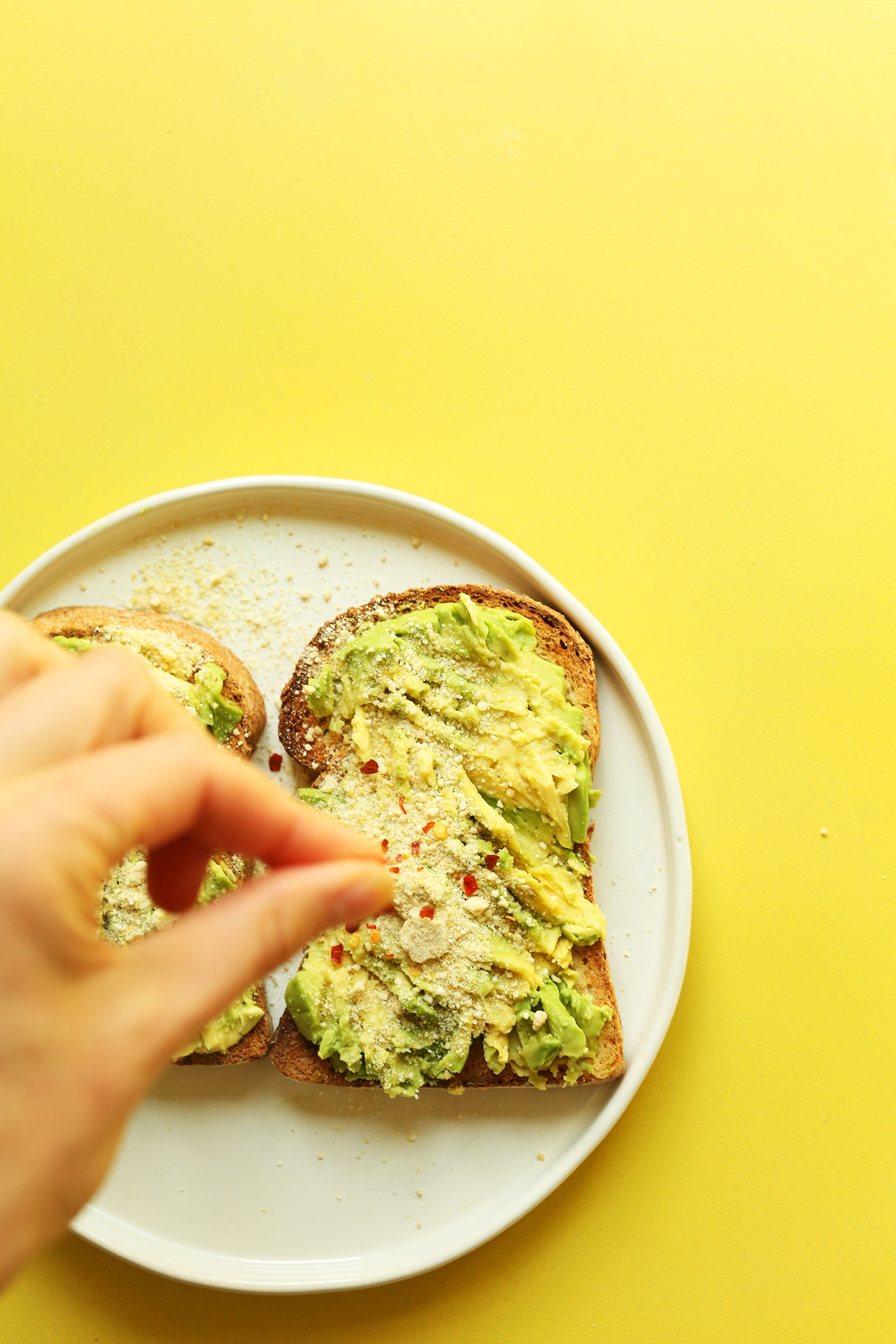 Sprinkling red pepper flake onto gluten-free avocado toast