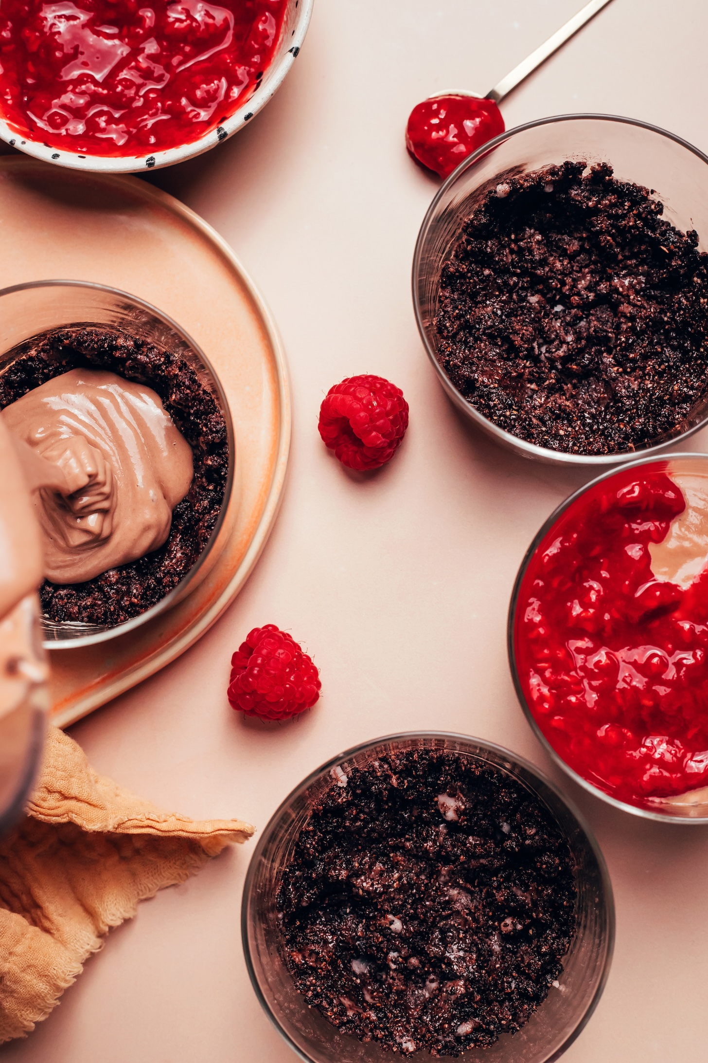 Pouring chocolate cheesecake filling into a glass dessert jar lined with a chocolate cookie crust