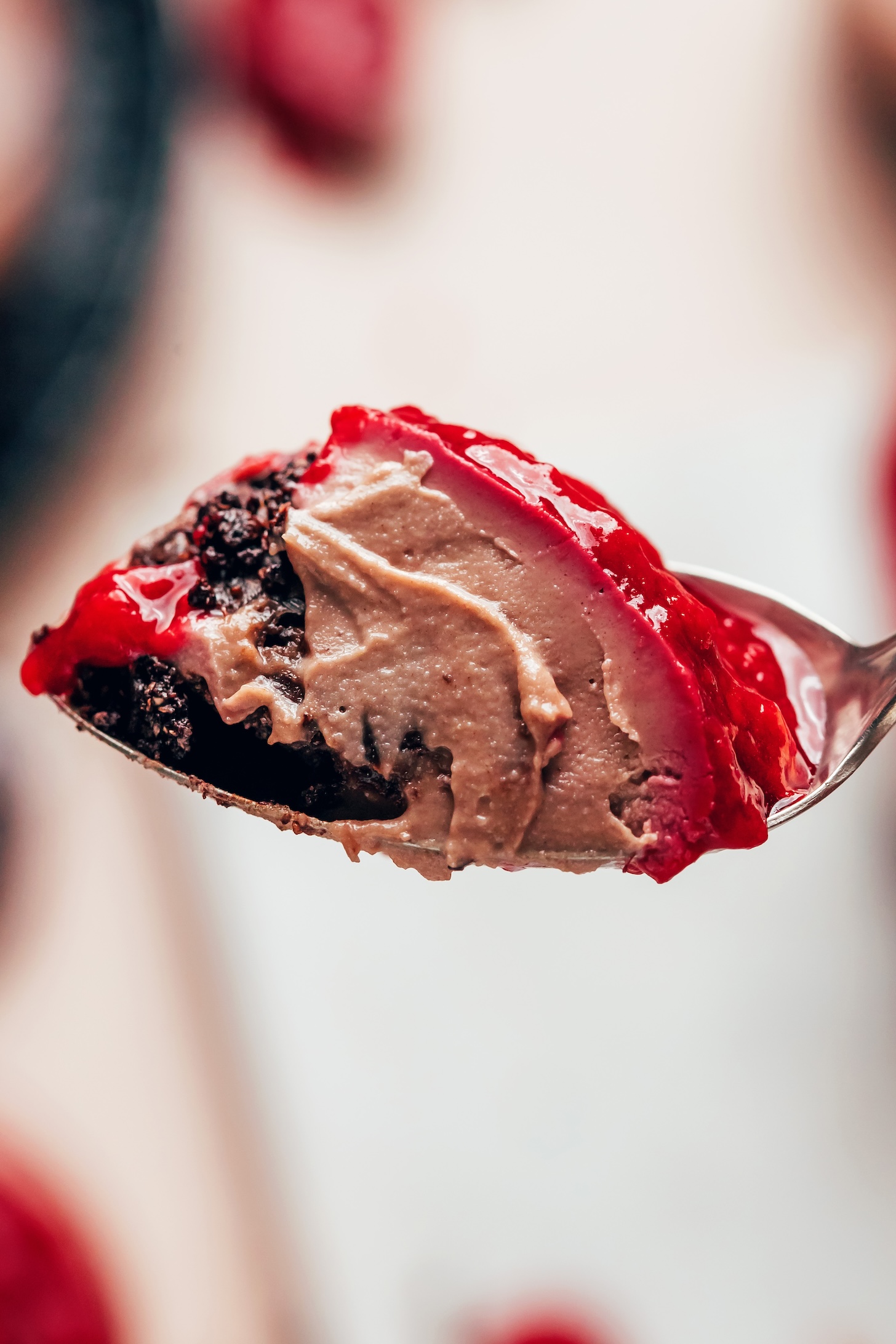 Close up photo of a bite of our no-bake cheesecake with a chocolate cookie layer, chocolate filling, and raspberry compote