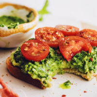 Slice of pesto avocado toast with fresh tomatoes