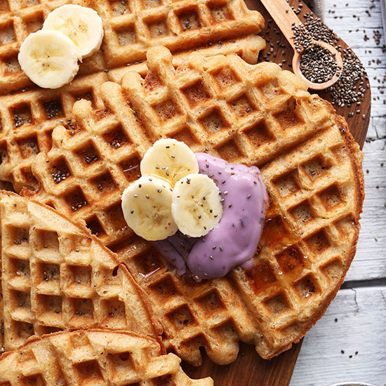 Cutting board with Coconut Yogurt Waffles topped with sliced banana and yogurt